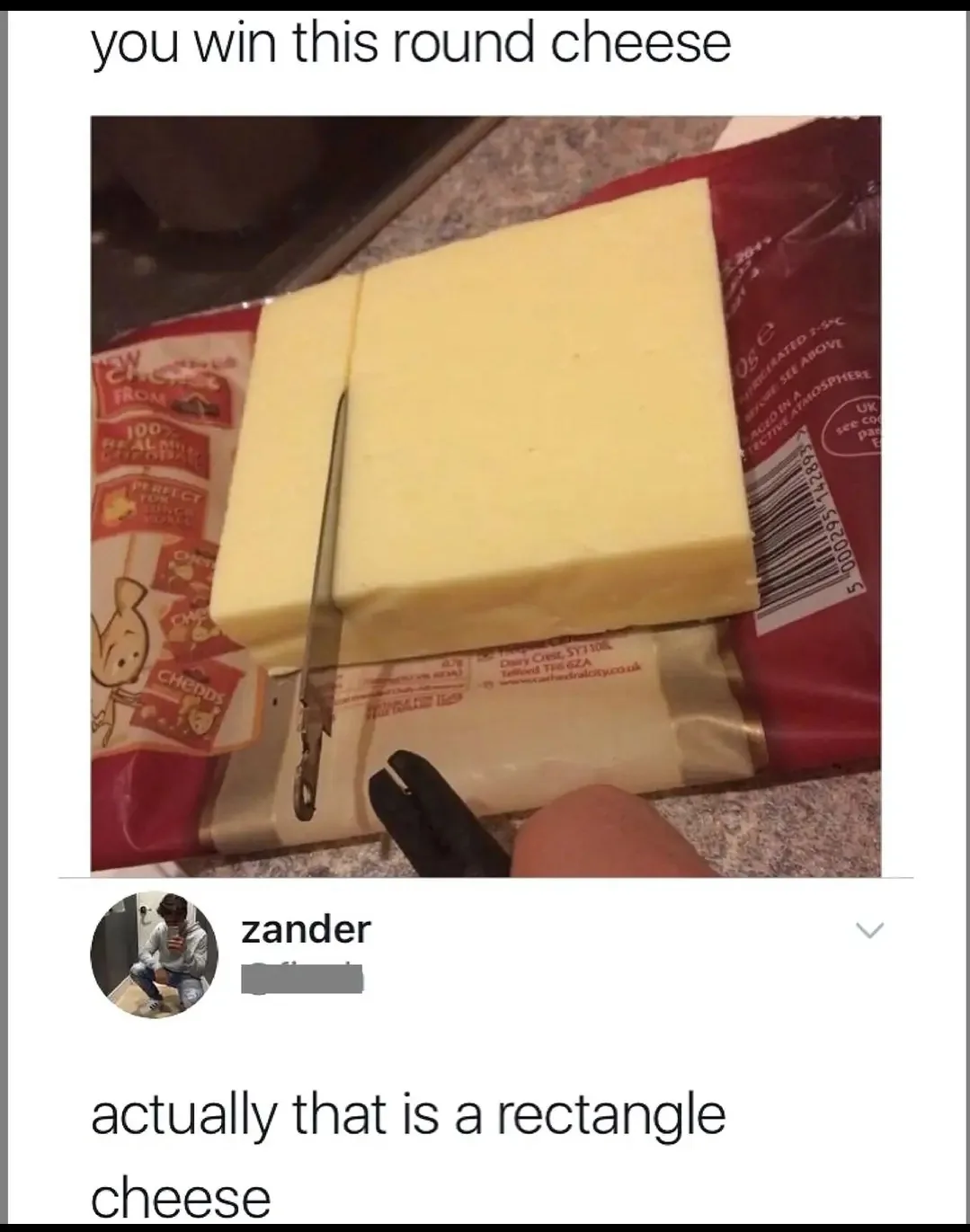 A block of cheese in a red wrapper is being cut with a knife, and a finger holds a black tool near the cut. The overlaid…