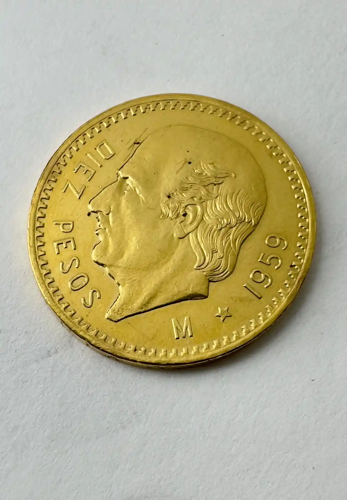 A close-up photo of a gold-colored coin featuring a profile of a man, with the text 'DIEZ PESOS' and '1959' visible around…