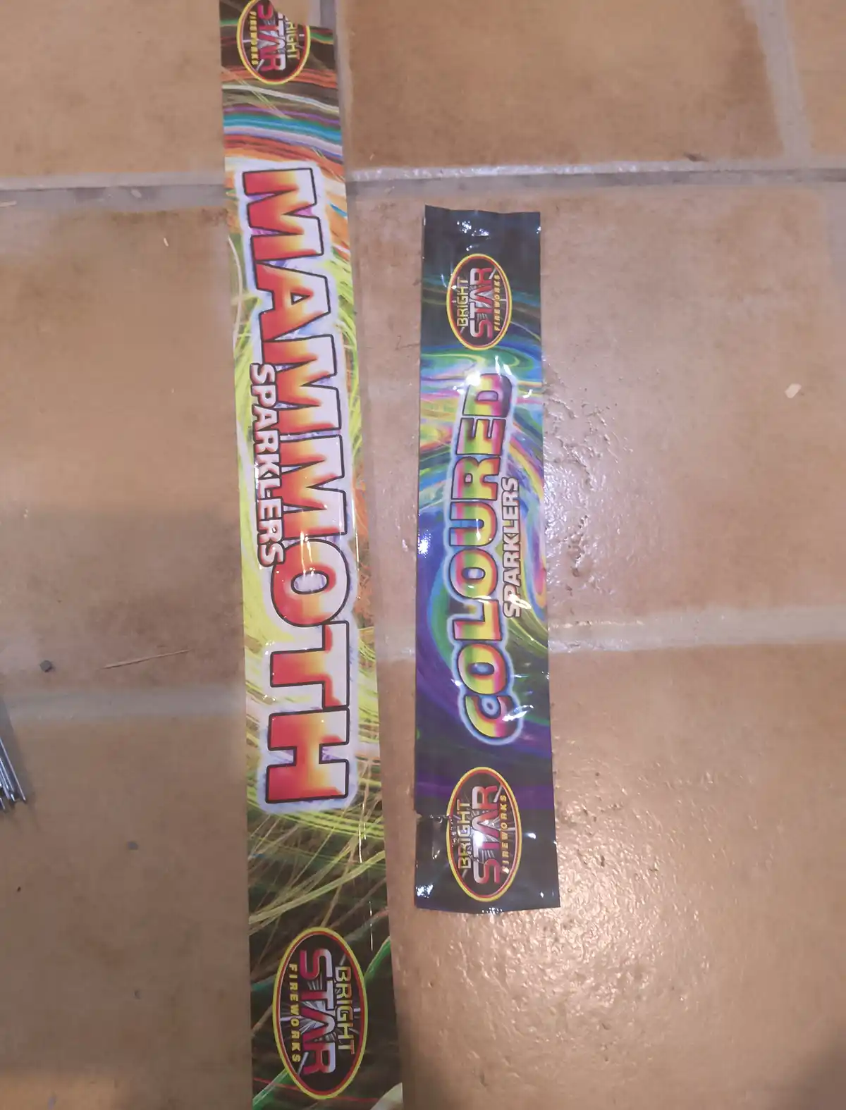 Two packages of Bright Star brand sparklers lie side by side on a tiled floor; one is labeled 'MAMMOTH SPARKLERS' and the…