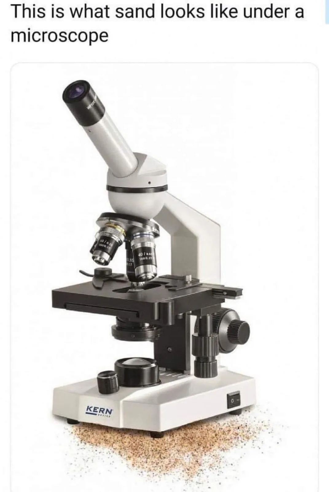 A white and black Kern Optics microscope is shown against a white background, with a small pile of sand grains scattered on…