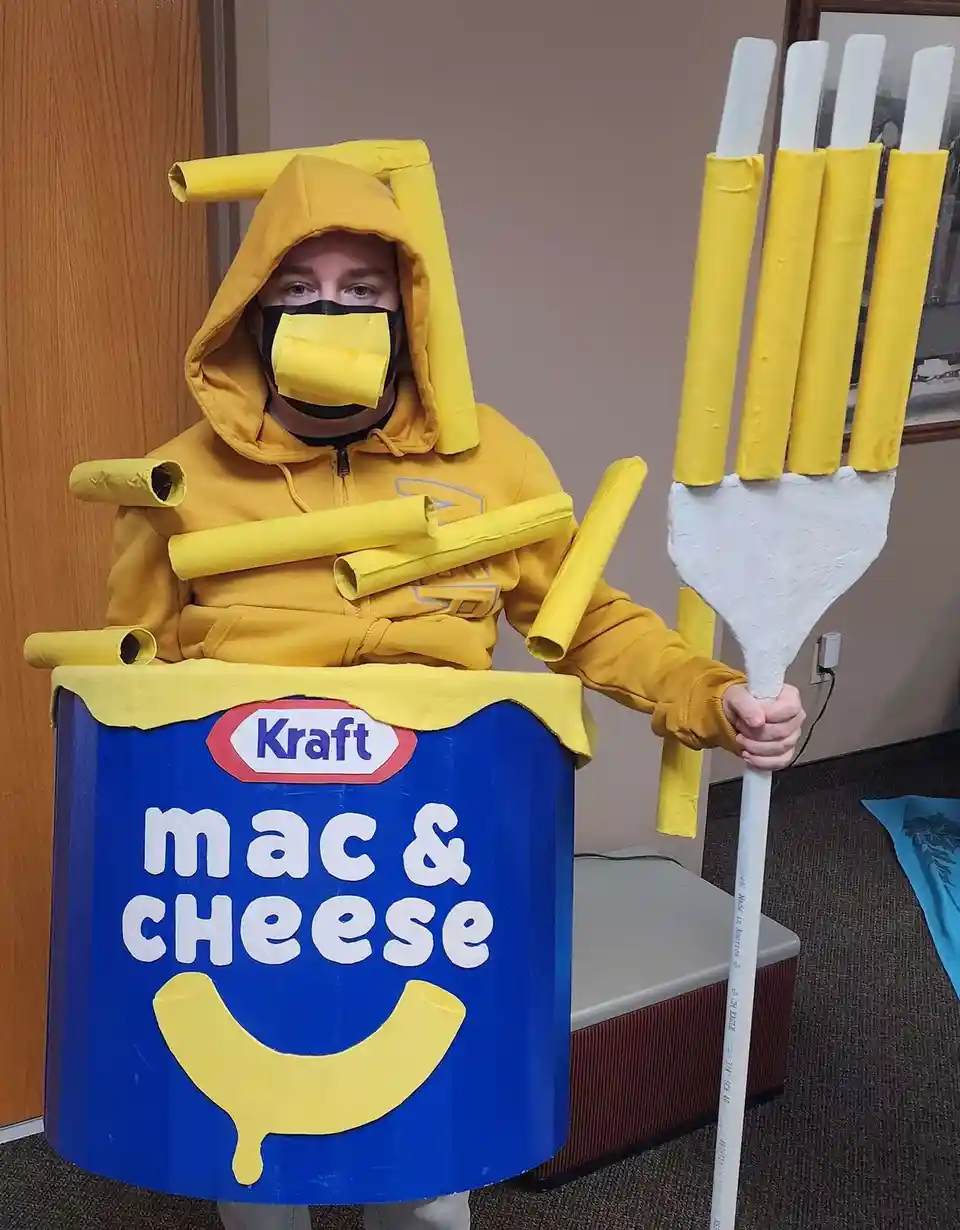 A person in a homemade costume is dressed as a Kraft Mac & Cheese box, with yellow paper tubes attached to their hood, arms…