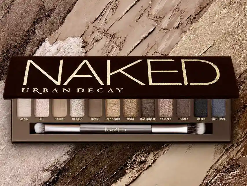 A close-up of the Urban Decay Naked eyeshadow palette, open to reveal ten neutral-toned shades labeled 'Virgin', 'Sin'…