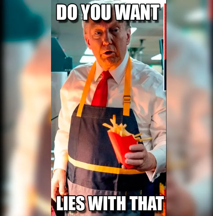 A man with gray hair, wearing a white shirt, red tie, and a dark blue apron with yellow straps, holds a red paper container…