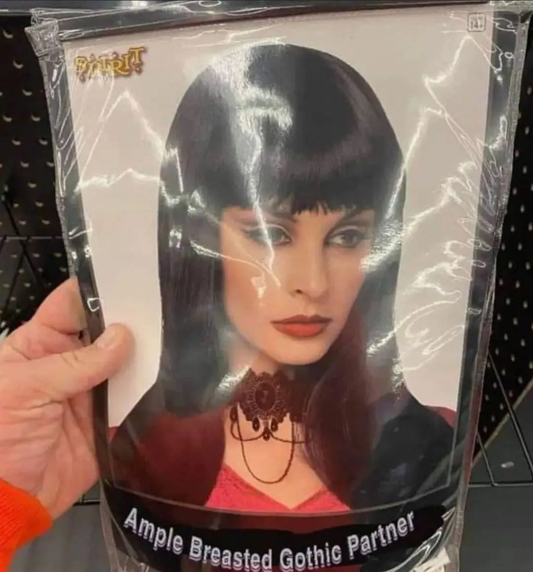 A hand holds a Spirit brand costume wig package featuring a woman with dark hair and bangs, wearing a choker and red top…