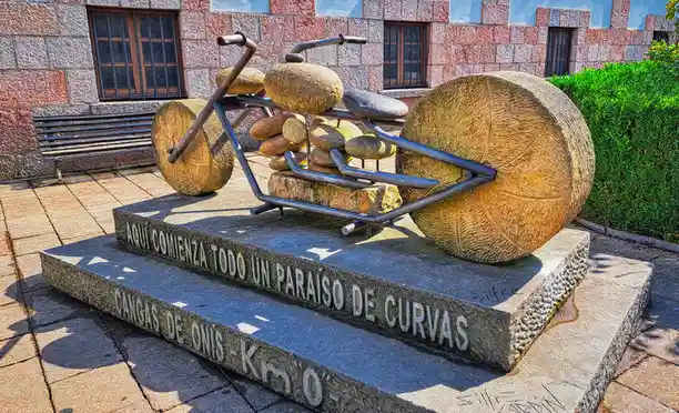 A stone sculpture of a bicycle made from large rounded stones and metal frames sits on a granite pedestal. The pedestal has…