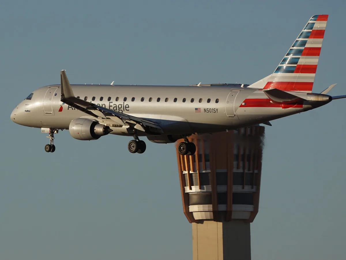An American Eagle airplane, registration N501SY, is captured in mid-flight with landing gear down, appearing to fly directly…