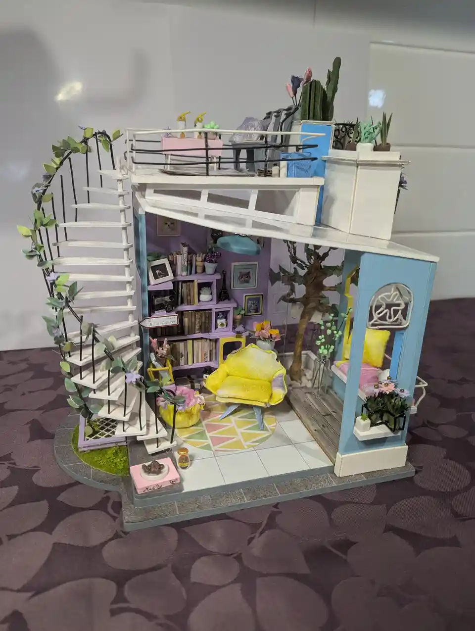 A detailed miniature dollhouse with a spiral staircase, colorful furniture, and numerous tiny plants and decorations inside…
