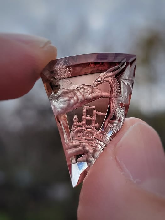 A close-up photo shows a person holding a small, translucent rose quartz crystal slice. The crystal has a detailed 3D…