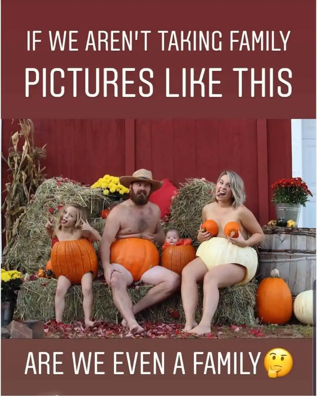 A family of four poses in front of a red barn, sitting on hay bales with pumpkins. The father, wearing a straw hat, sits…