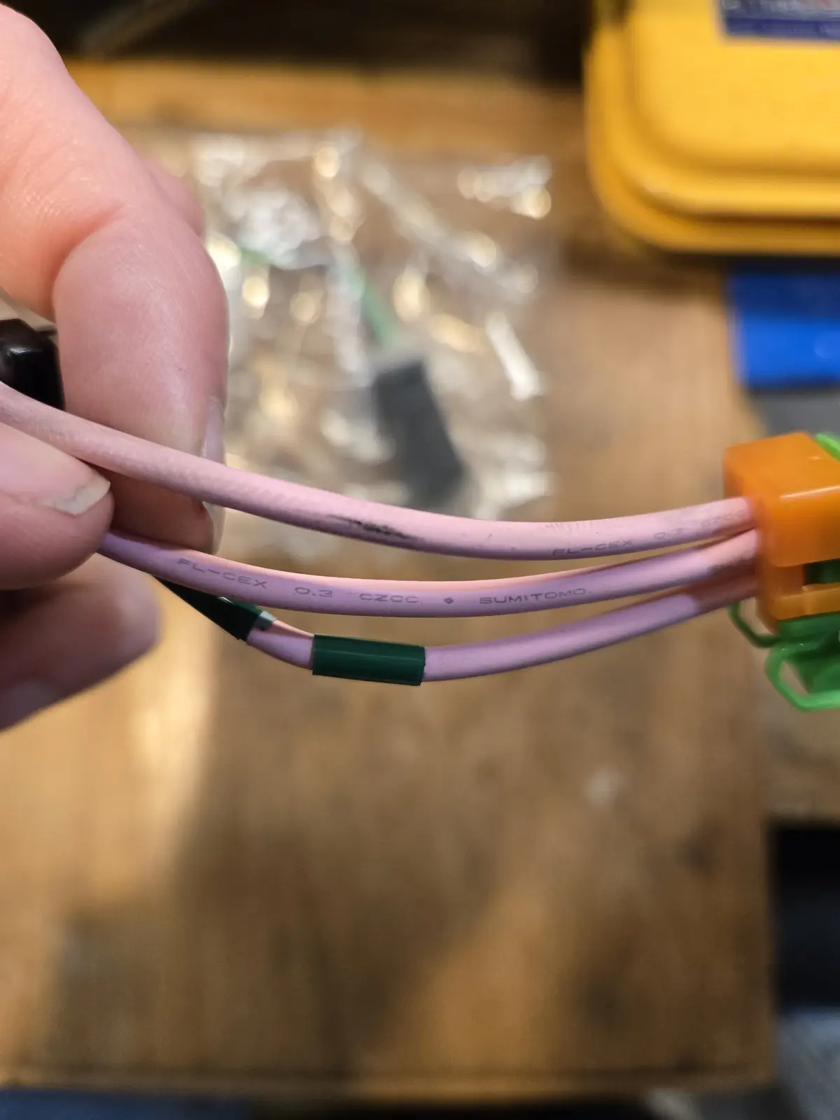 A close-up photo shows a hand holding three light pink electrical wires with printed text, one of which has a green heat…