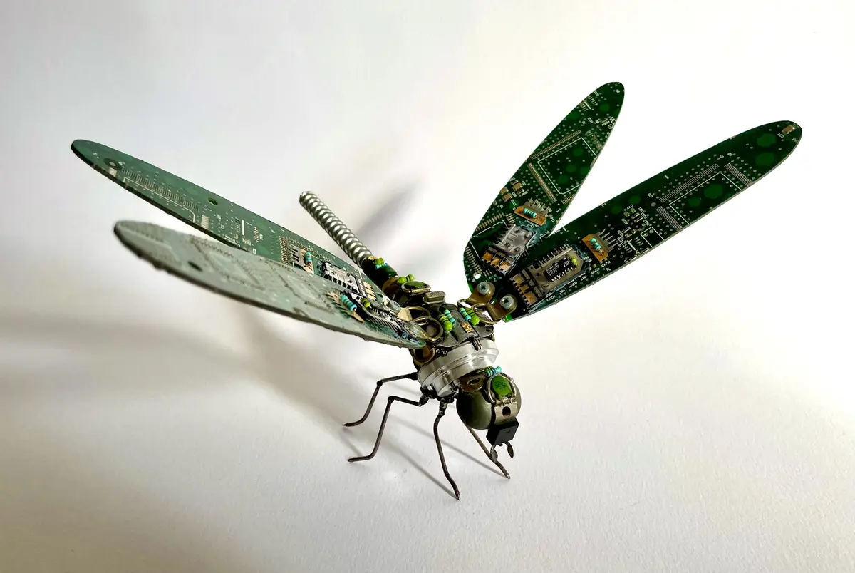 A dragonfly sculpture crafted entirely from green circuit boards for wings, metal components for the body and legs, and…