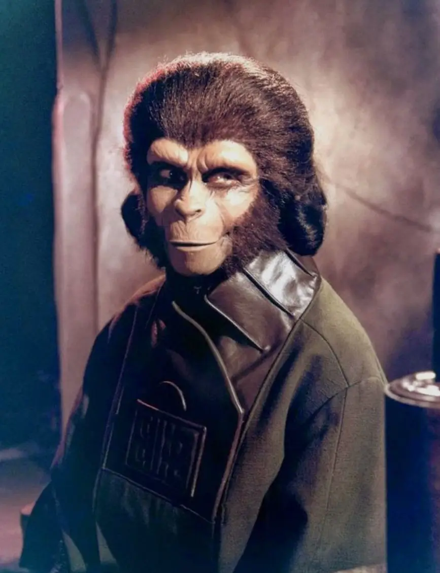 A still image from the movie 'Planet of the Apes' shows a chimpanzee in a dark, futuristic uniform with a name tag, looking…