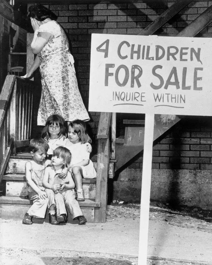A black-and-white photo shows four children sitting on wooden steps while a woman stands on the stairs behind them. A large…