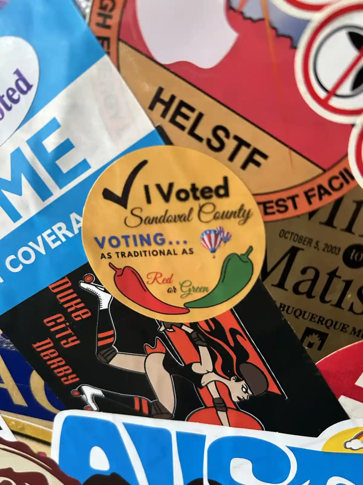 A close-up photo shows a yellow circular 'I Voted' sticker from Sandoval County, featuring a checkmark, text, and…