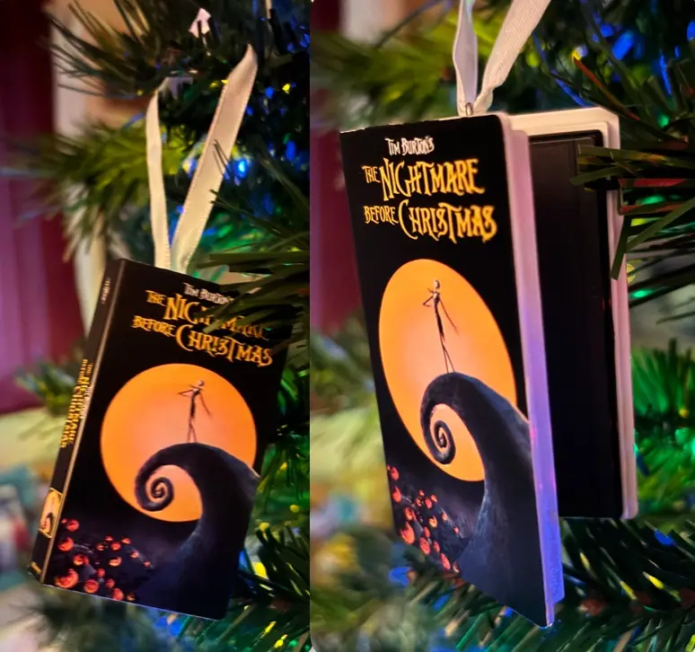 Two photos show a Christmas ornament shaped like a VHS tape of 'The Nightmare Before Christmas,' hanging on a lit tree. The…