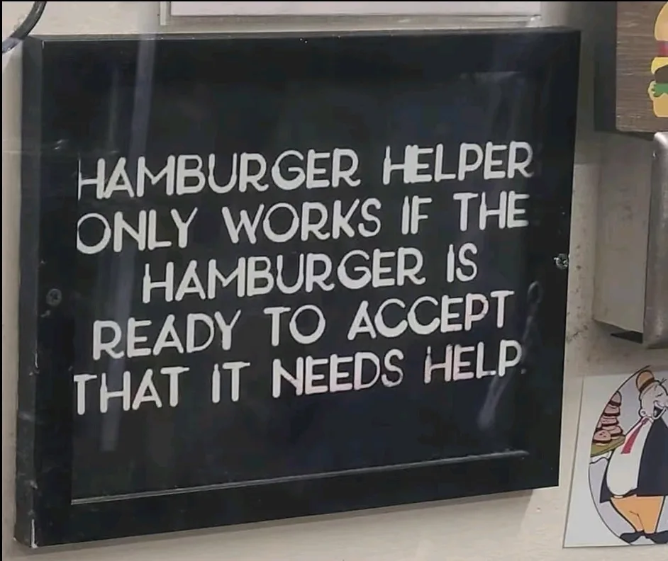 A black sign with white, blocky text reads 'HAMBURGER HELPER ONLY WORKS IF THE HAMBURGER IS READY TO ACCEPT THAT IT NEEDS…