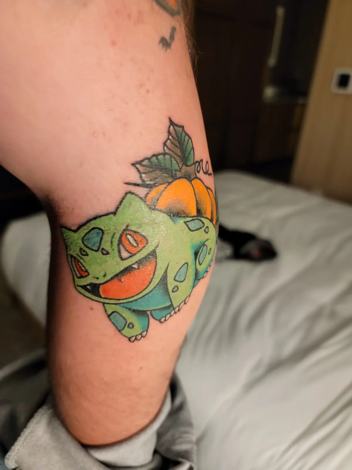 A close-up photo shows a colorful tattoo on a person's upper arm, depicting the Pokémon Bulbasaur with a pumpkin growing…