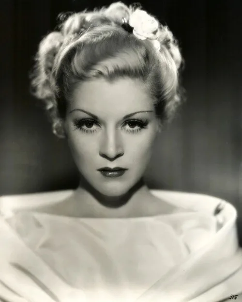 A vintage black-and-white portrait of a woman with styled blonde hair adorned with a white flower, wearing a light-colored…