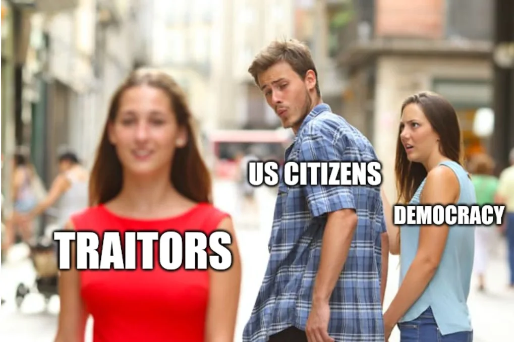 A man in a blue plaid shirt stands on a city street, turning his head to look at a woman in a red top labeled 'TRAITORS'…