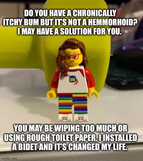 A lego minifigure with brown hair, glasses, and a rainbow-striped outfit stands in front of a yellow object. The overlaid…