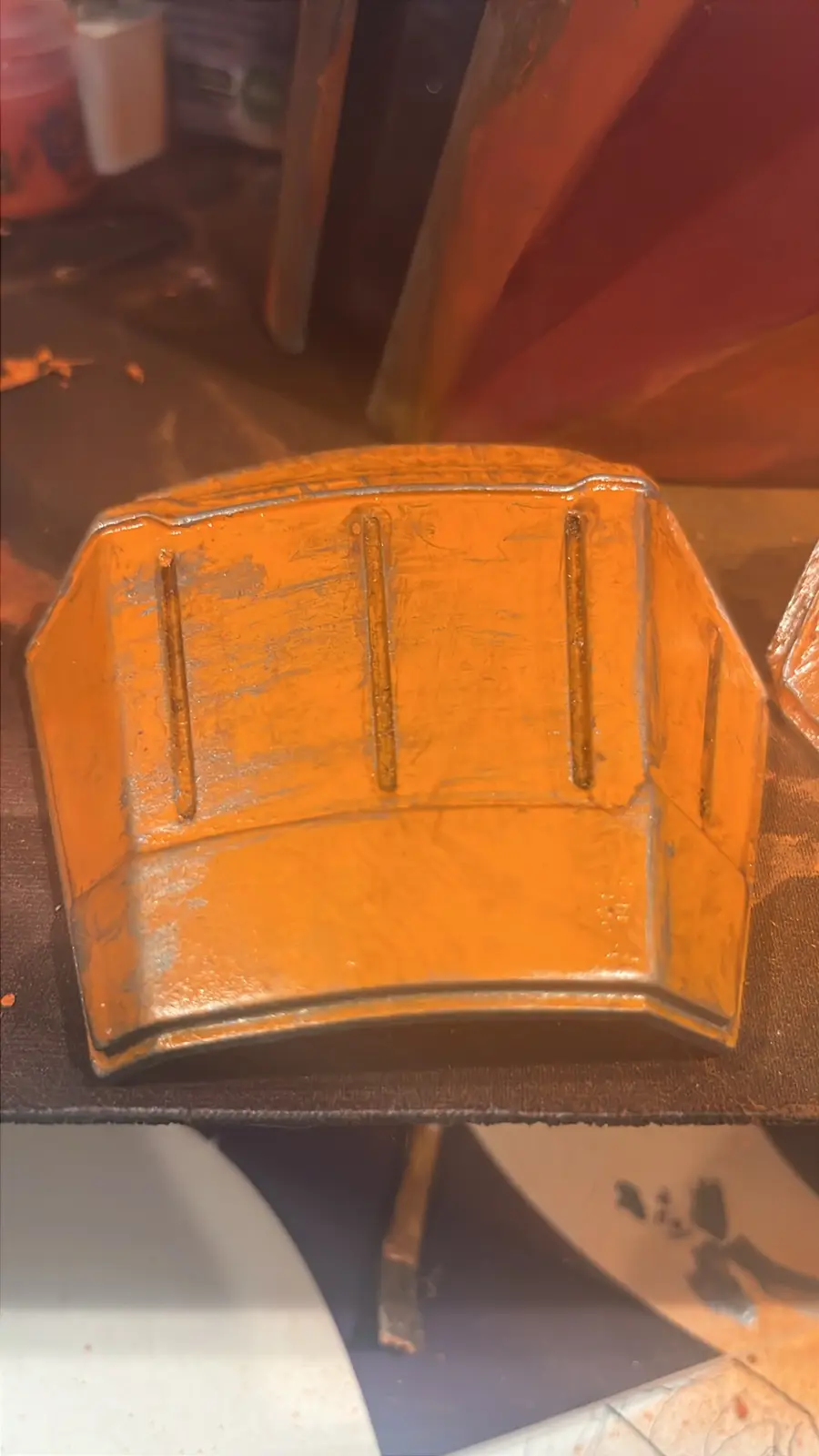 A close-up photo shows a custom-painted orange motorcycle helmet, viewed from the top, revealing its worn paint and vertical…
