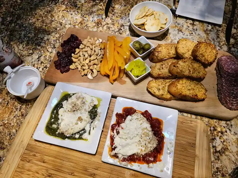 A wooden cutting board displays an elaborate charcuterie and appetizer spread, including dried cranberries, cashews, yellow…