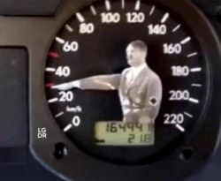 A close-up of a car's speedometer shows a man in a suit pointing at the 40 mph mark. The speedometer reads 40 mph, and the…