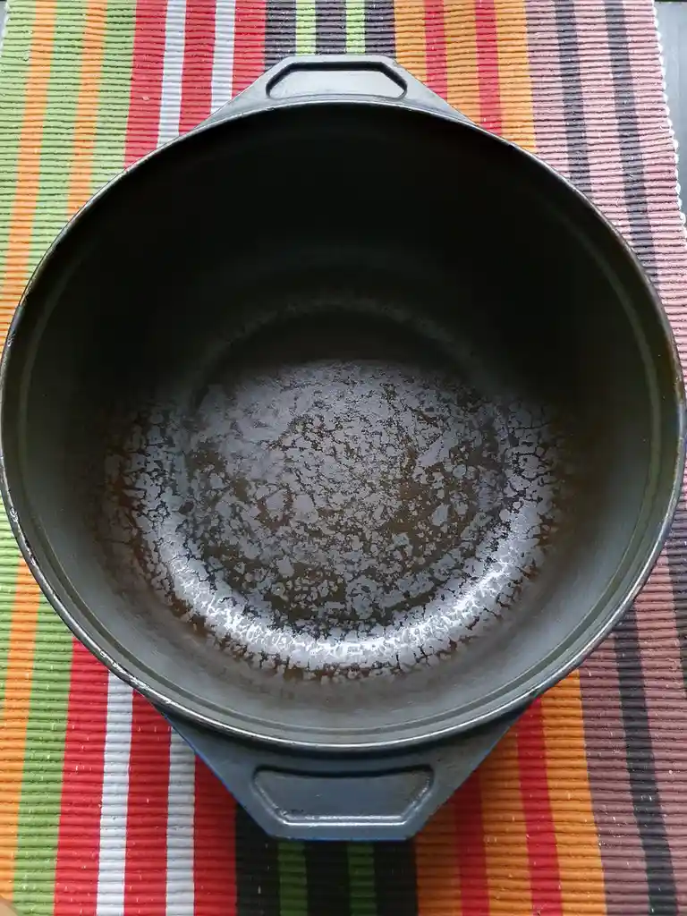 An overhead shot of a well-used, dark gray cast iron skillet resting on a colorful striped placemat. The bottom of the pan…
