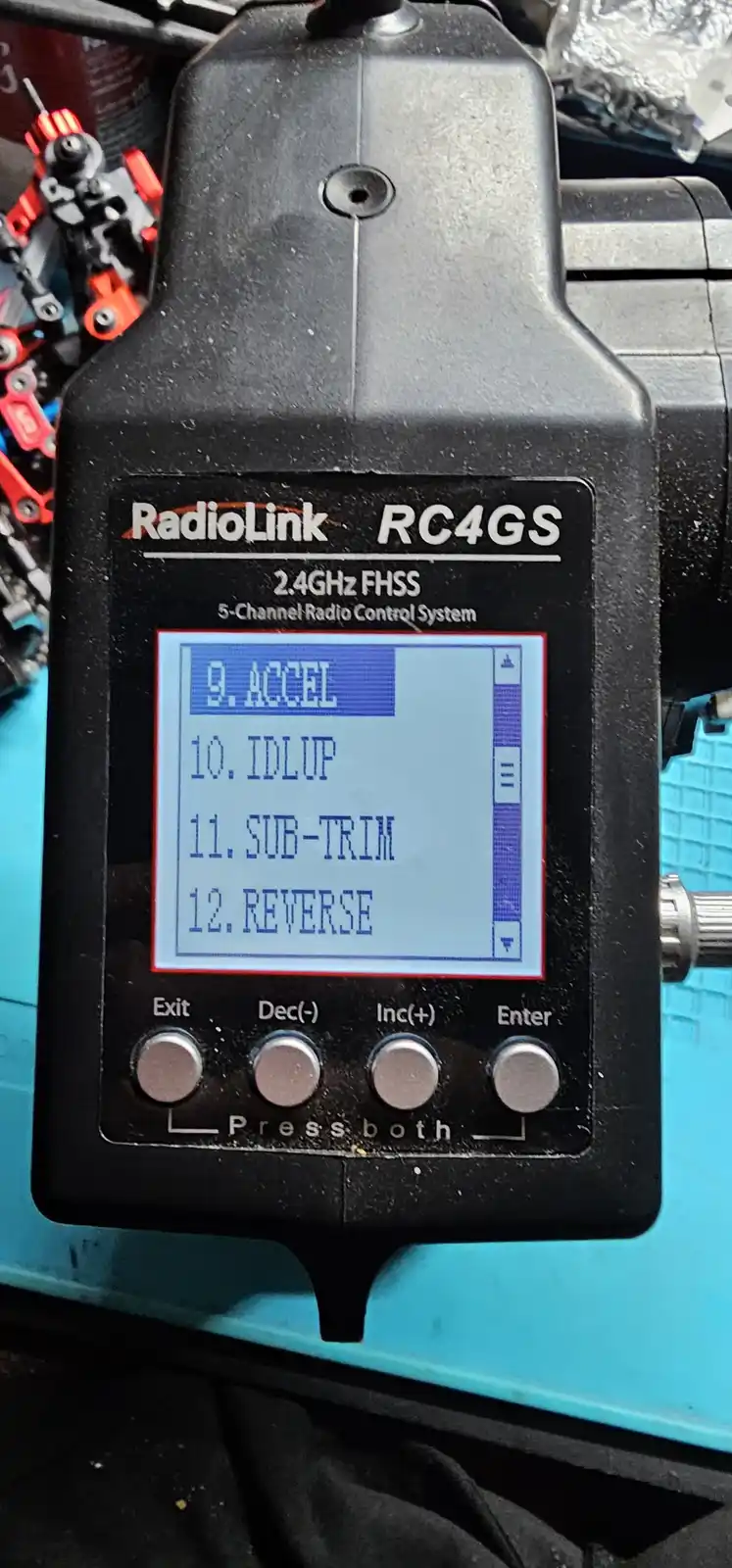 A close-up of a black RadioLink RC4GS 5-channel radio control transmitter with a small LCD screen displaying menu options 9…