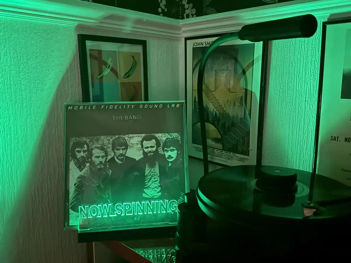 A vinyl record player sits next to a 'Mobile Fidelity Sound Lab' album cover for 'The Band', which has glowing green text…