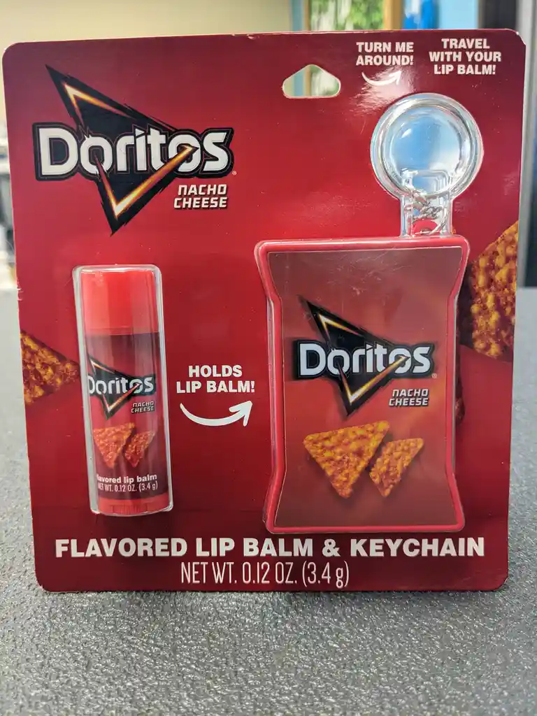 A red Doritos Nacho Cheese branded package contains a small lip balm tube and a keychain shaped like a Doritos chip bag. The…