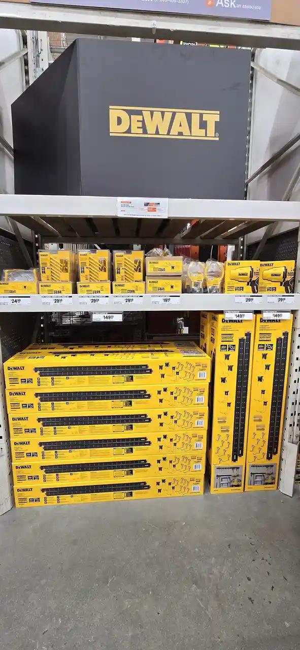 A large black DeWalt box sits on a store shelf above stacks of yellow DeWalt tool storage boxes, with the overlaid text 'de…