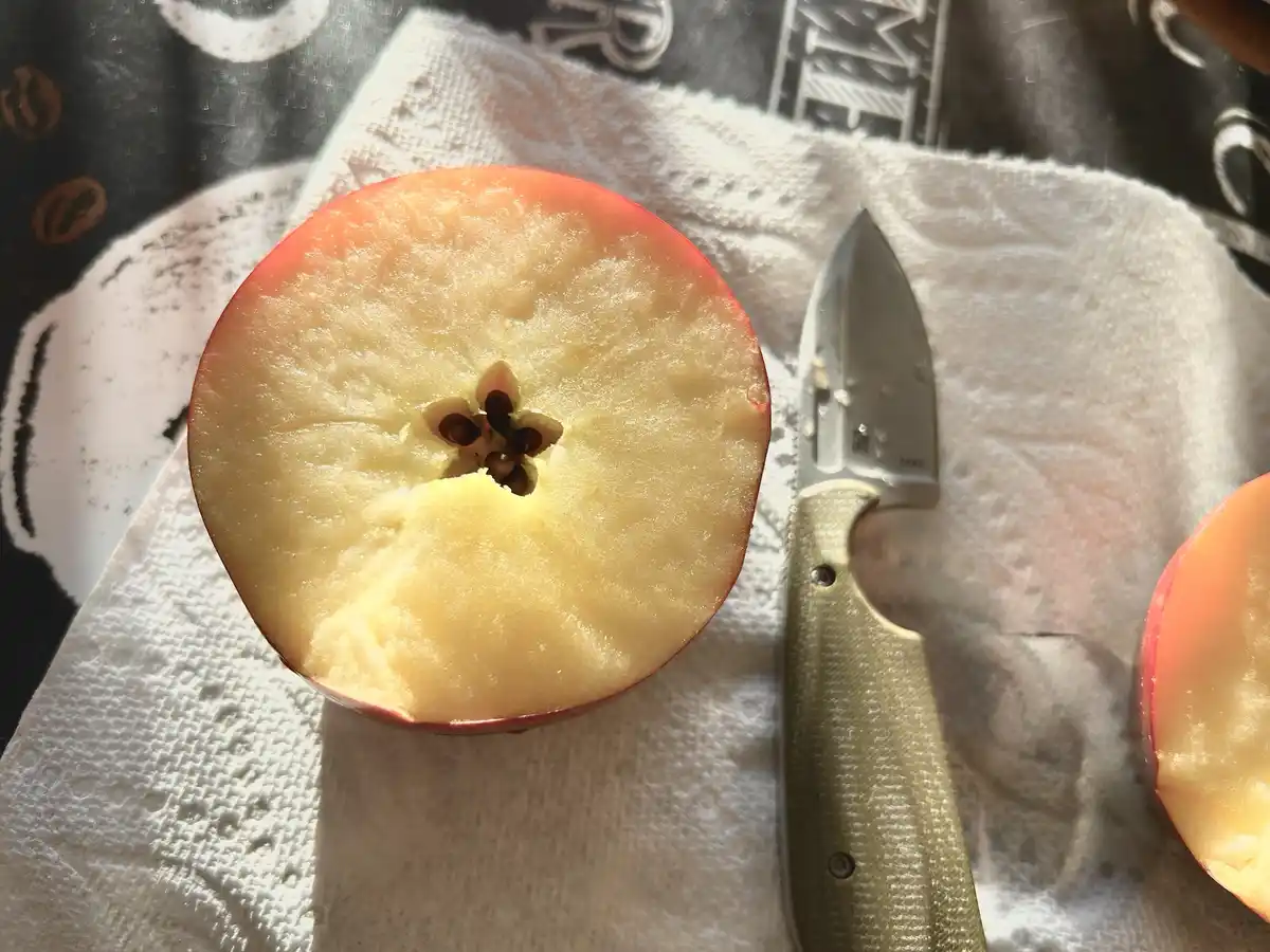 A sliced red apple with its core and seeds visible sits on a white paper towel next to a small knife, with the overlaid text…