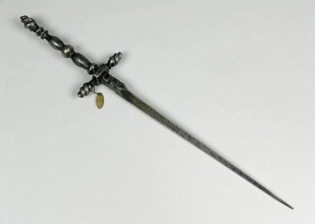 a close-up photograph of an ornate, antique dagger with a decorative twisted hilt and a long, slender blade, lying…