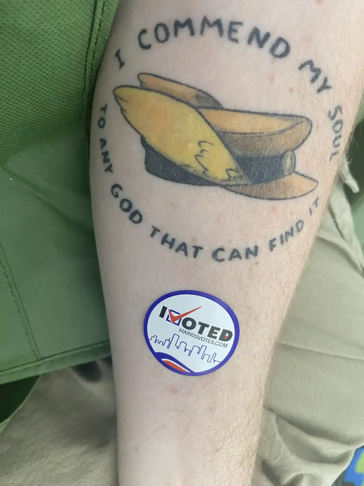 A close-up of a person's forearm showing a tattoo of a yellow and black hat with the text 'I COMMEND MY SOUL TO ANY GOD THAT…