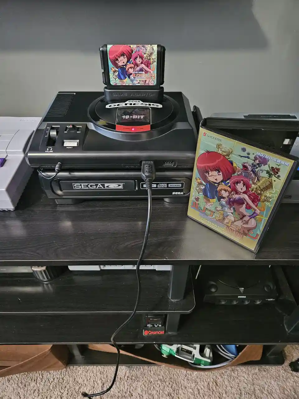 A Sega Genesis console with a Game Adaptor inserted, displaying the game 'Panorama Cotton' on its screen, next to the game's…