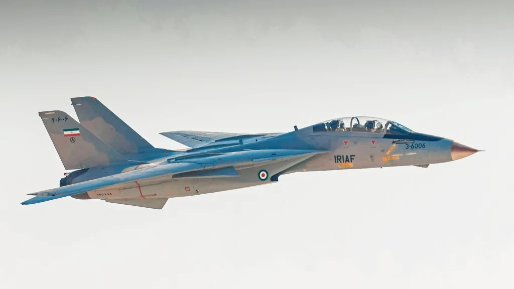 A grey Iranian Air Force fighter jet, marked with 'IRIAF' and tail number '3-6006', is shown in flight against a plain sky…