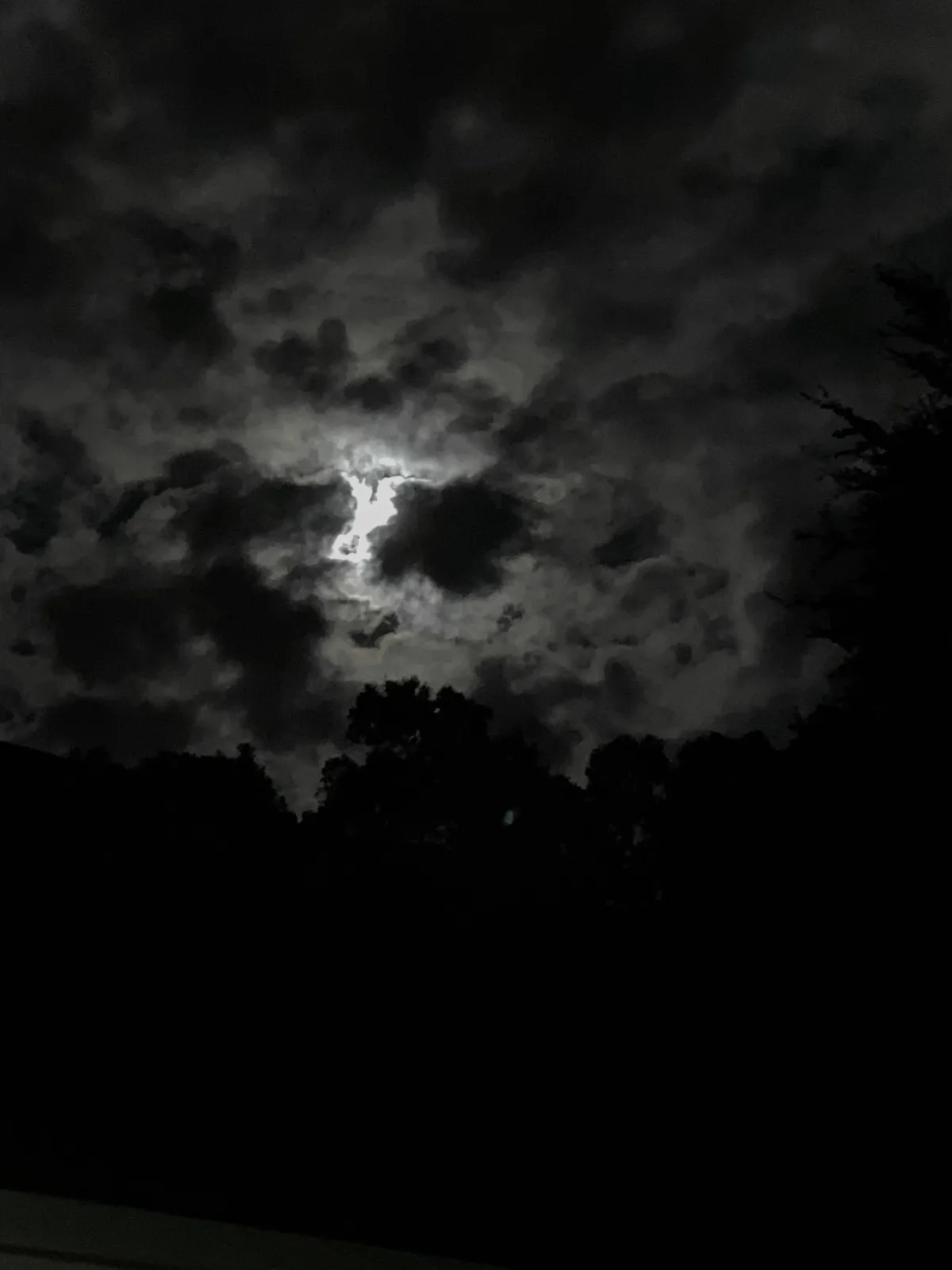 A night sky photo shows a bright moon partially obscured by dark clouds, with the clouds' shape resembling a bat silhouette…