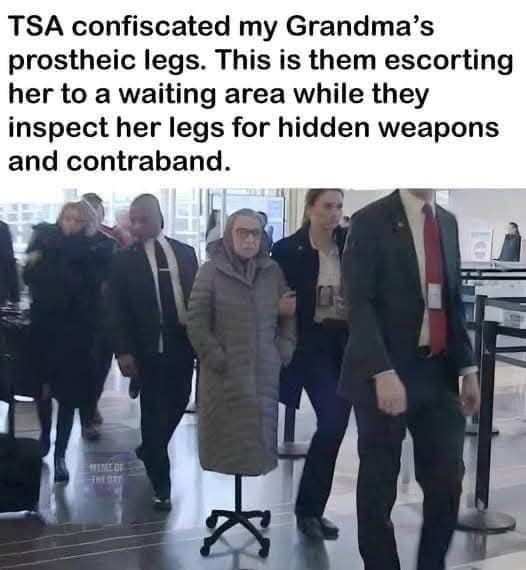 An elderly woman in a grey coat is being escorted by TSA agents through an airport security checkpoint. Her prosthetic legs…