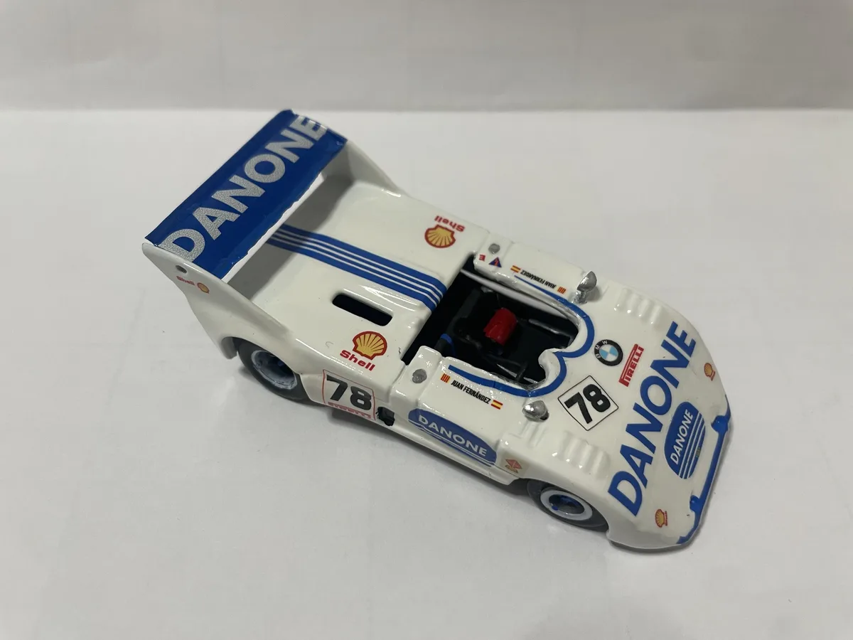 A white and blue scale model of a vintage race car, likely a BMW, is shown on a plain white surface. The car is covered in…