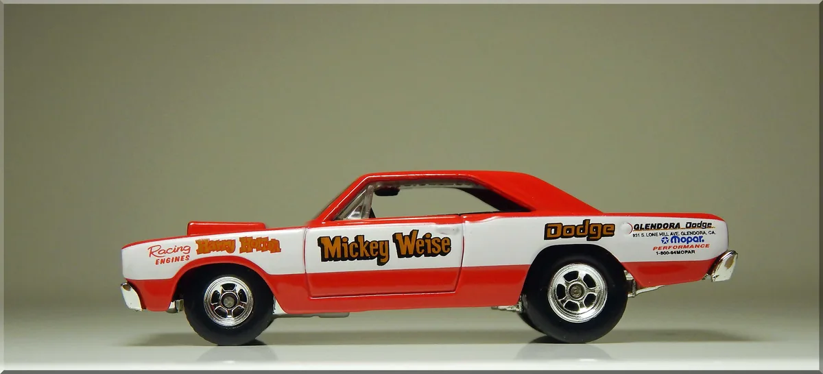 A red and white die-cast model of a classic Dodge race car, shown in profile against a plain background. The car features…
