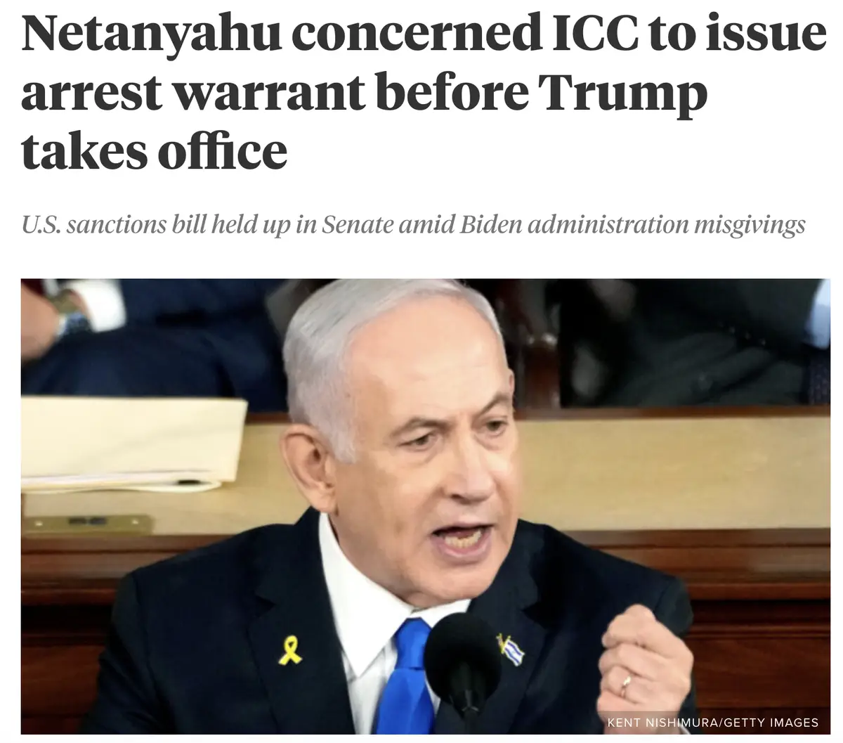 A photo of Benjamin Netanyahu speaking at a podium, wearing a dark suit, white shirt, and blue tie, with a yellow ribbon and…