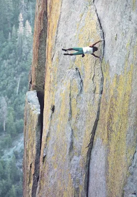 A person is suspended horizontally against a steep rock face, appearing to be in mid-air with arms and legs spread out. The…