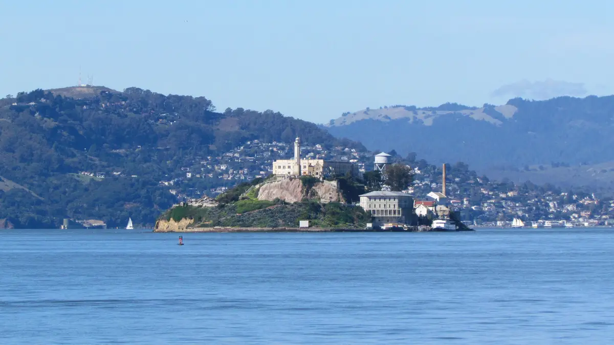 A scenic view of Alcatraz Island in San Francisco Bay, featuring its historic prison buildings, a lighthouse, and…