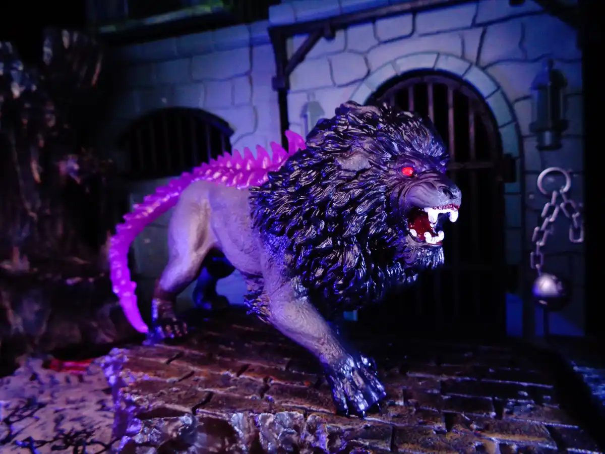 A toy lion figurine with glowing red eyes and a bright purple spiky tail stands aggressively on a stone platform in front of…