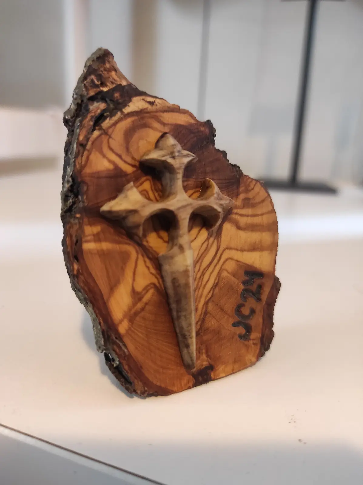 A close-up of a wooden sculpture featuring a carved cross embedded in a slice of wood with visible grain patterns and bark…