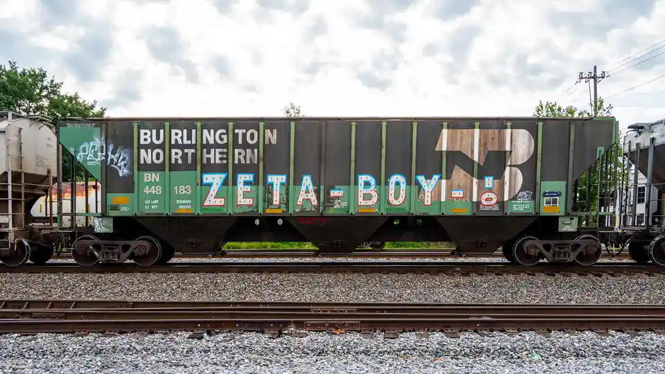 A Burlington Northern freight train car, number BN 448 183, is covered in graffiti, prominently featuring the text…