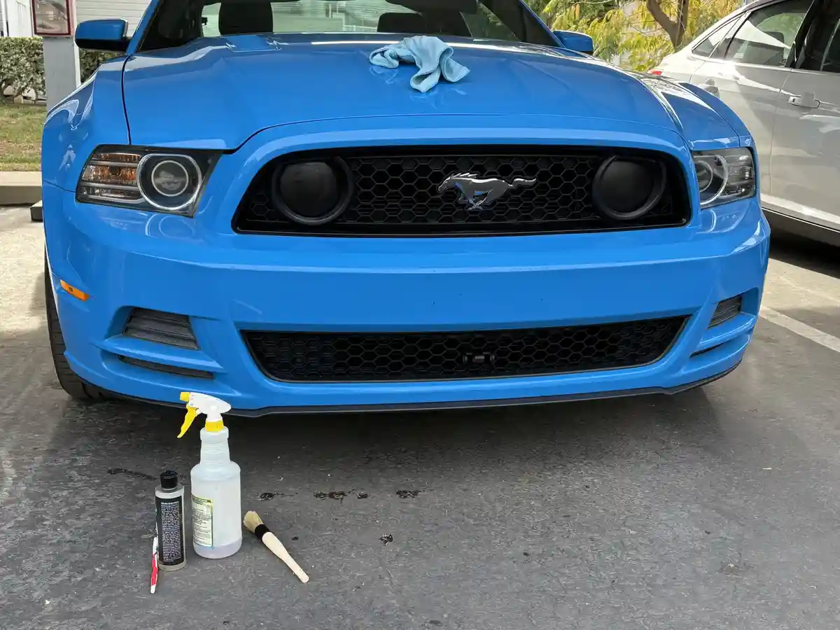 A bright blue Ford Mustang is shown from the front, with a light blue microfiber cloth resting on its hood. In front of the…