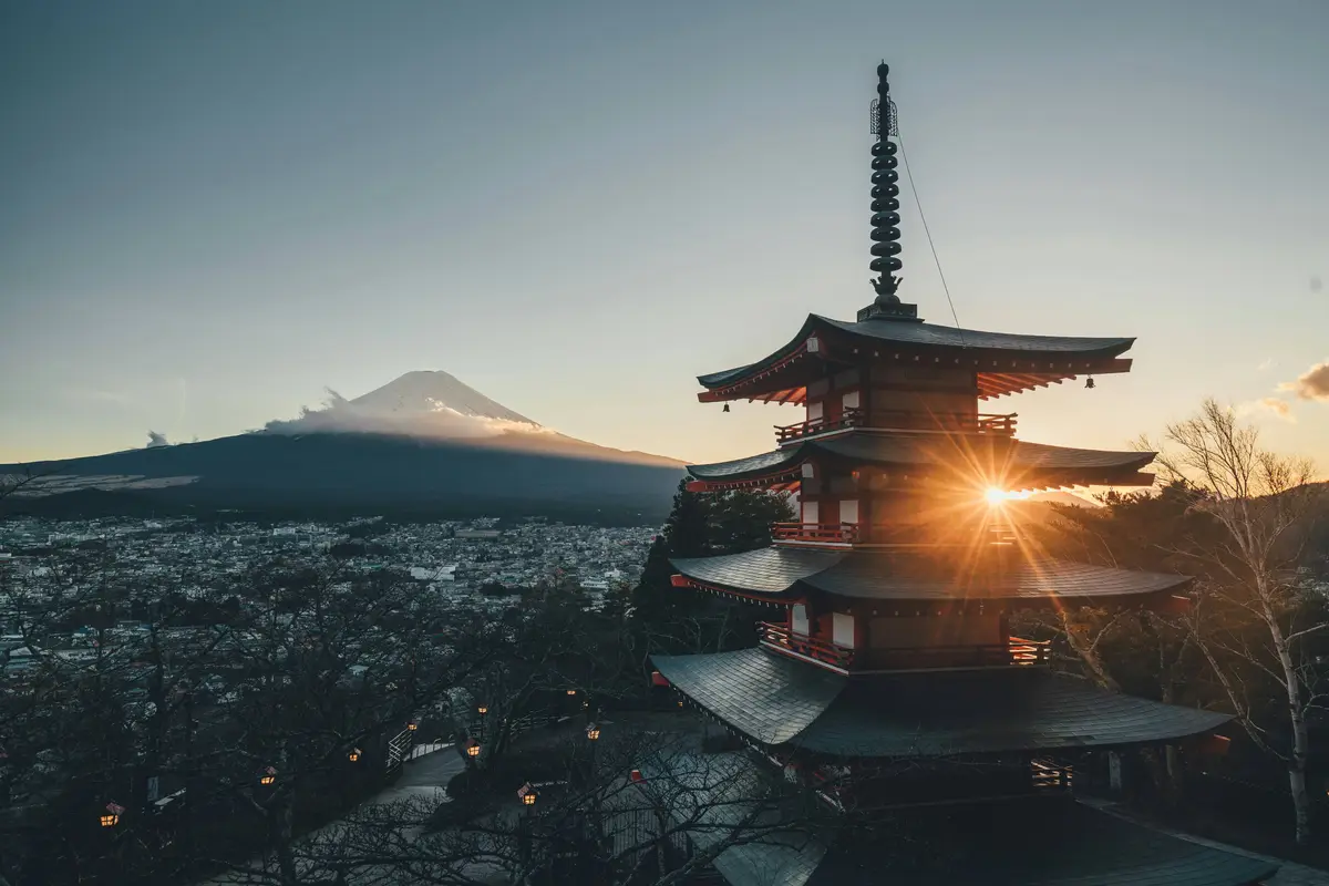 A serene photograph shows a traditional Japanese pagoda with multiple tiered roofs, silhouetted against a setting sun that…
