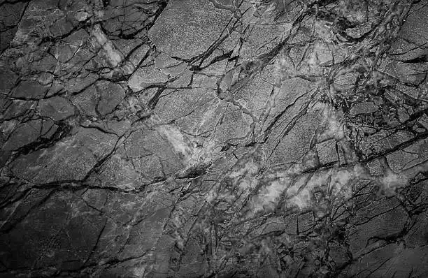 A black-and-white image of a cracked, textured surface resembling dried mud or fractured stone. Overlaid text in white reads…